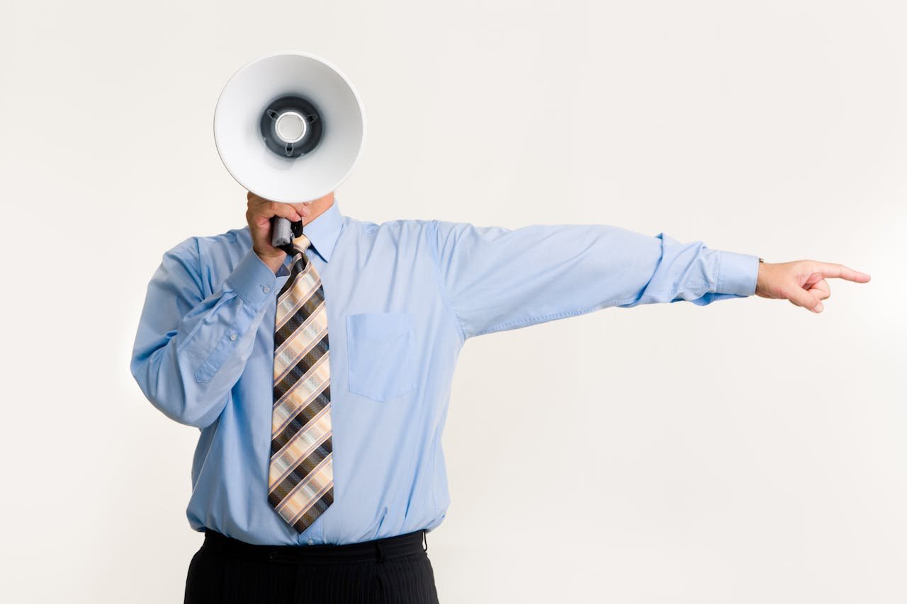 Businessman in blue shirt using a megaphone while pointing, isolated on white background.